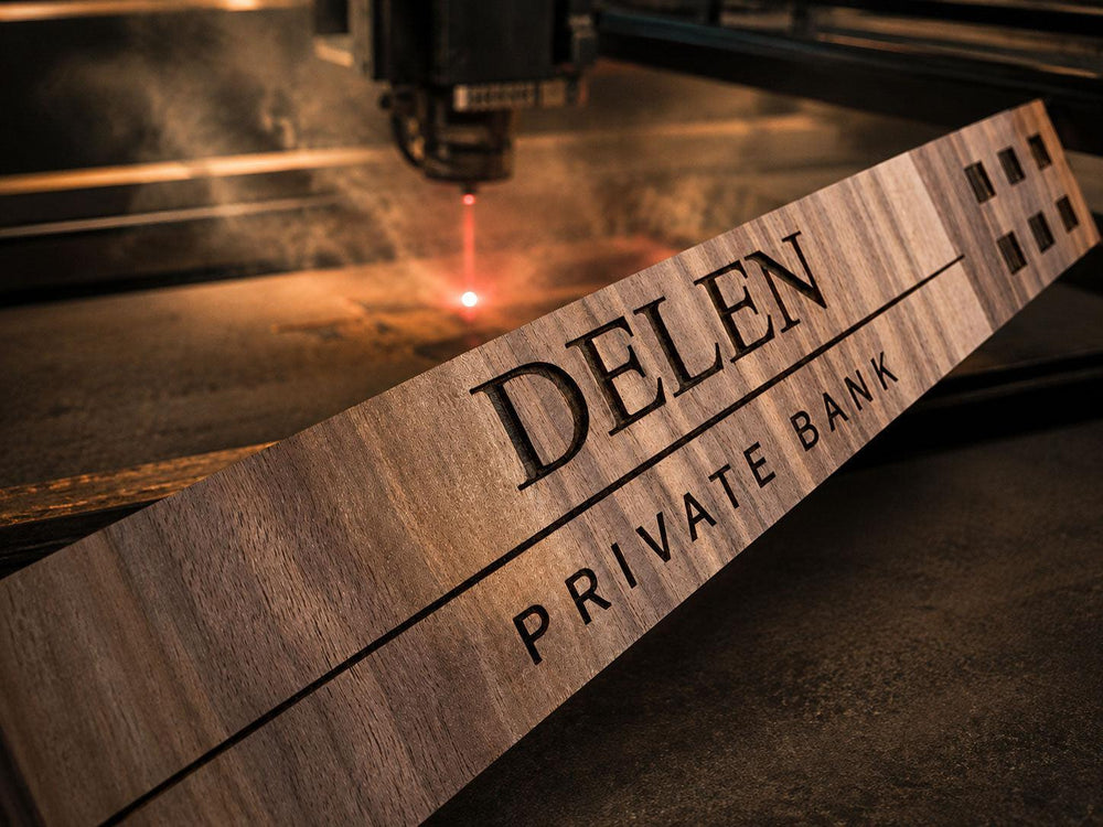 Laser graveert het logo van Delen Private Bank in een houten plank, met gloed en rookpluim